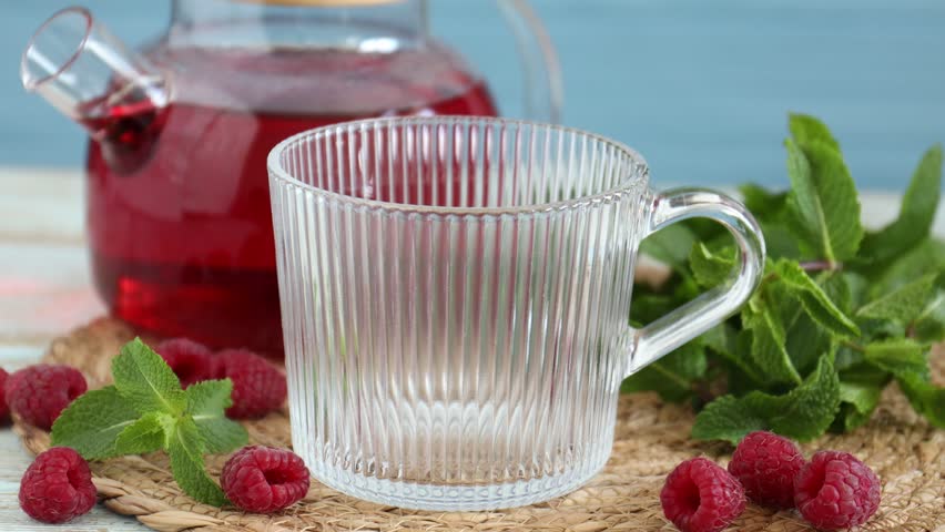 Woman pouring aromatic raspberry tea into glass cup at wooden table, closeup