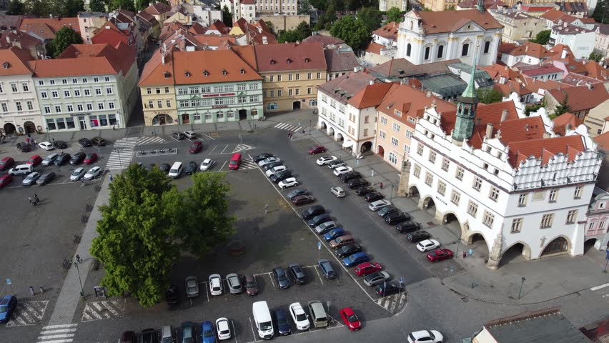 An aerial view of the historic town square in Litomeerice, Czech Republic, showing red-roofed buildings, parked cars, and open plaza