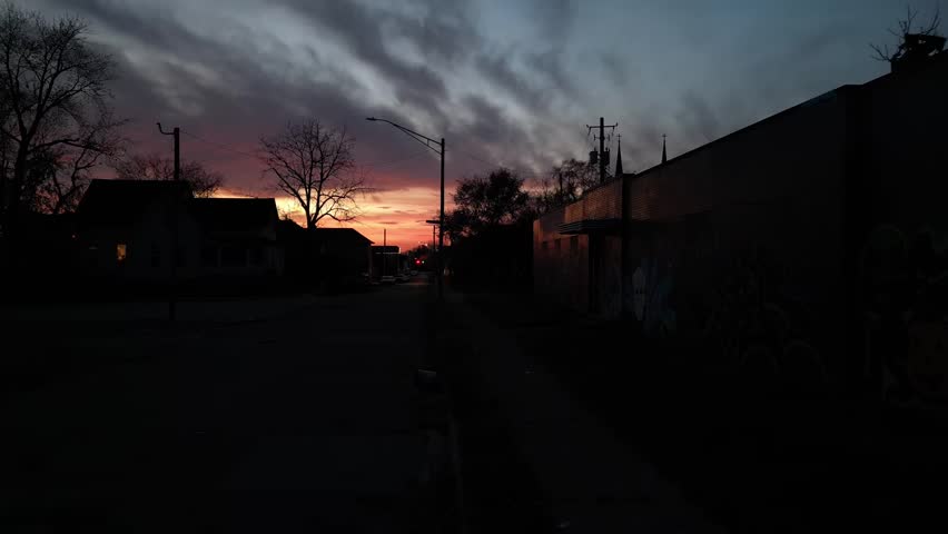 A breathtaking sunset over a quiet urban street, with silhouettes of buildings and bare trees against a dramatic, colorful sky in Indianapolis