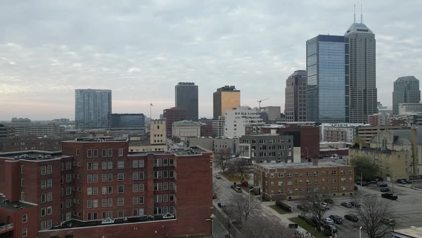A drone perspective of central Indianapolis highlighting the city skyline with diverse architecture beneath a calm overcast sky