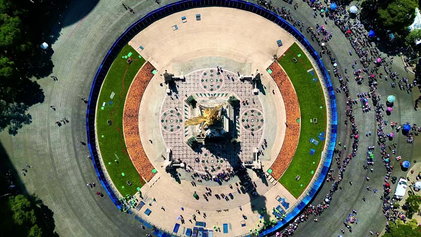 An aerial shot of circular square with the Angel of Independence monument, surrounded by walking paths, trees and crowd of people in Mexico City