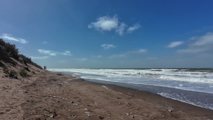 Windy day on a deserted beach with strong waves rolling onto the sandy shore under a blue sky