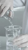 Unknown scientist wearing a lab coat and gloves is carefully pouring a liquid from a beaker into an Erlenmeyer flask, close up. Science and medicine - Powered by Shutterstock - Get 15% off with code: PIKWIZARD15