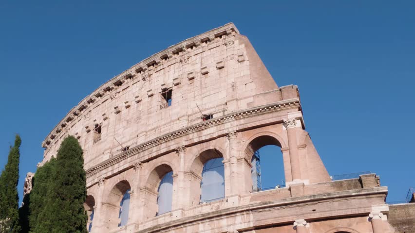 Close-up view of the iconic Colosseum in Rome, Italy, showcasing its ancient Roman arches and weathered stone facade beneath a clear blue sky on a sunny day.