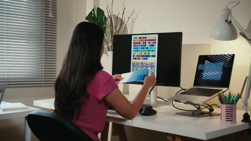 Creative graphic designer choosing colors from a swatch for a new project. Young woman artist working at her desk in a modern office