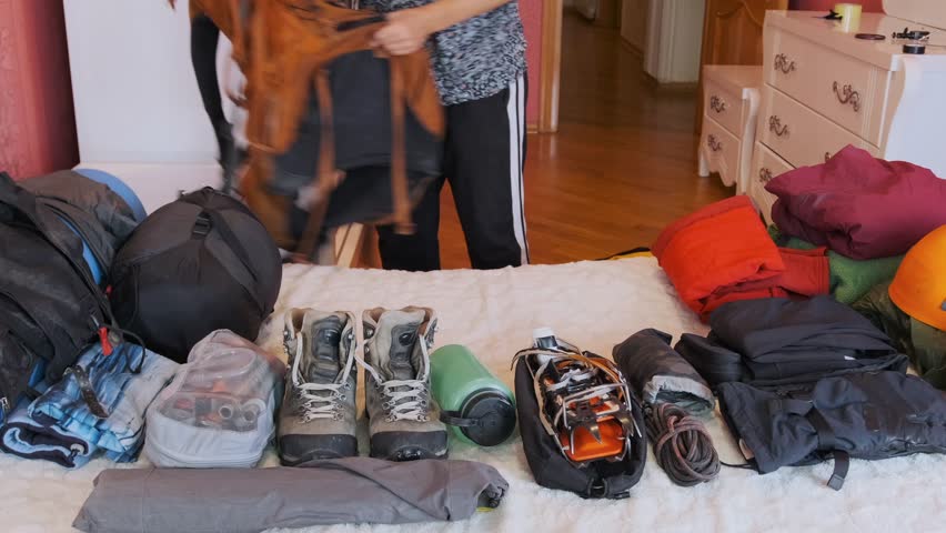 Woman packing climbing backpack with gear at home, preparing equipment for hiking or mountaineering trip, organizing items on table, travel preparation, adventure planning and outdoor activity setup