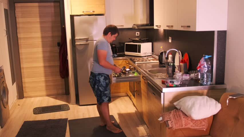 Man placing cutlery into sliding kitchen drawer, organizing forks spoons and knives in modern kitchen, everyday household routine, maintaining order cleanliness and functional storage at home