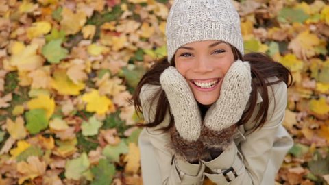 Fall woman excited and happy with autumn leaves falling. Cheerful and joyful smiling girl enjoying fall foliage with a smile. Beautiful young mixed race Asian Caucasian female model