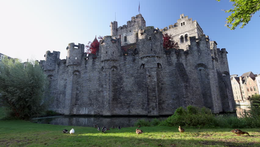 Gravensteen, a medieval castle in the city of Ghent in Belgium, Europe. Majestic Medieval Fortress with Moat and Ducks on Lush Green Grass, Historical European Castle