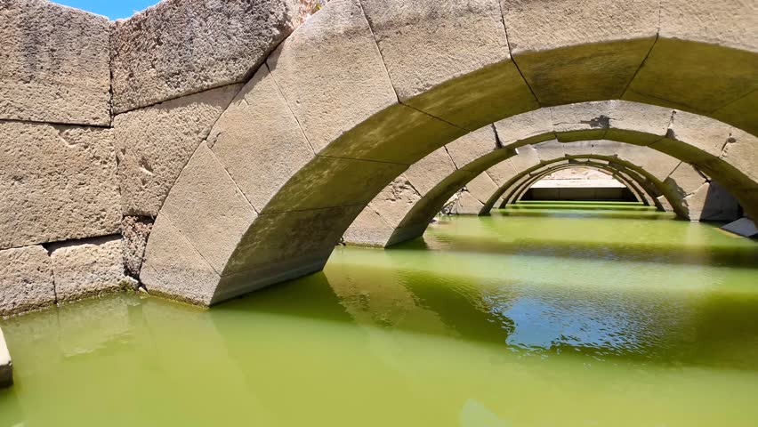 Ancient stone arches and vaulted corridors are partially submerged in green standing water at Claros archaeological site in Turkey.