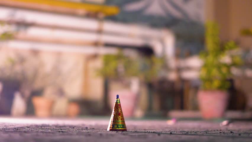 Close-up of a person using a sparkler to light an anar fountain firework during Diwali celebrations at night, with glowing flames and smoke with blurred background of a house