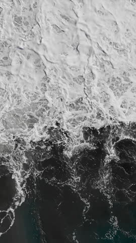 Atlantic waves crashing onto rocky pebble coast, dynamic ocean motion from drone above water