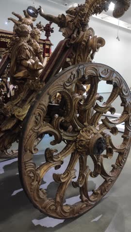 Close-up of a luxury antique royal carriage with intricate golden wood carvings, ornate wheels, and red velvet interior, exhibited in a museum. Historical vintage transportation of royalty