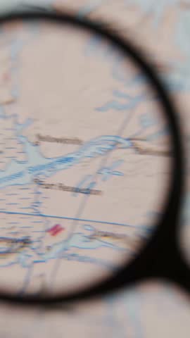 A hand-held magnifying glass moves across a paper map of Trondheim, focusing on a marked location. The area under the glass is highlighted for viewing.