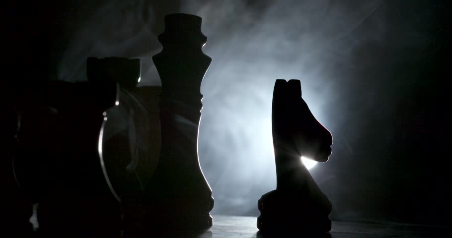 Silhouettes of chess pieces are dramatically illuminated against a smoky background, creating a mysterious and intriguing ambiance in an artistic presentation.