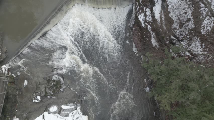 Overhead winter scene showing icy gray river currents winding through snow-dusted natural terrain