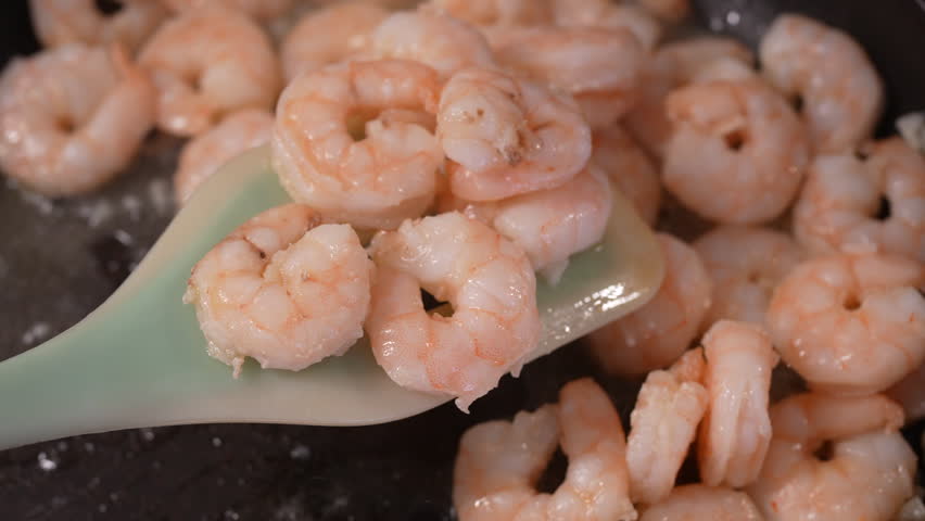 4K slow-motion video of lifting fried prawns on a spatula and stirring them in a pan