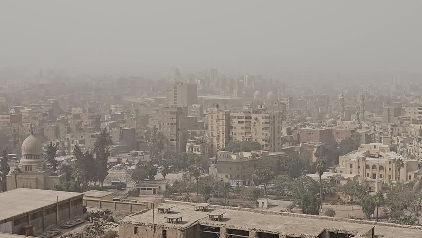 Two grand Cairo mosques with multiple minarets and imposing domes rise above the sprawling hazy cityscape of Egypt