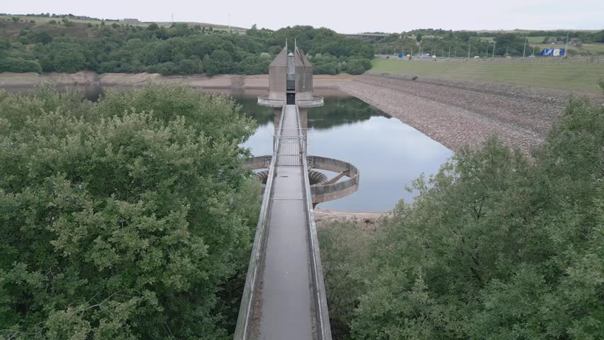 An An aerial view of a modern dam bridge extending over still reservoir waters surrounded by green hills