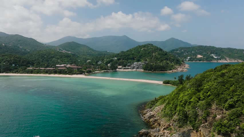 Aerial view of sandy beach meeting turquoise sea and surrounded by lush green hills. Ko Ma Beach. Ko Pha Ngan, Thailand.