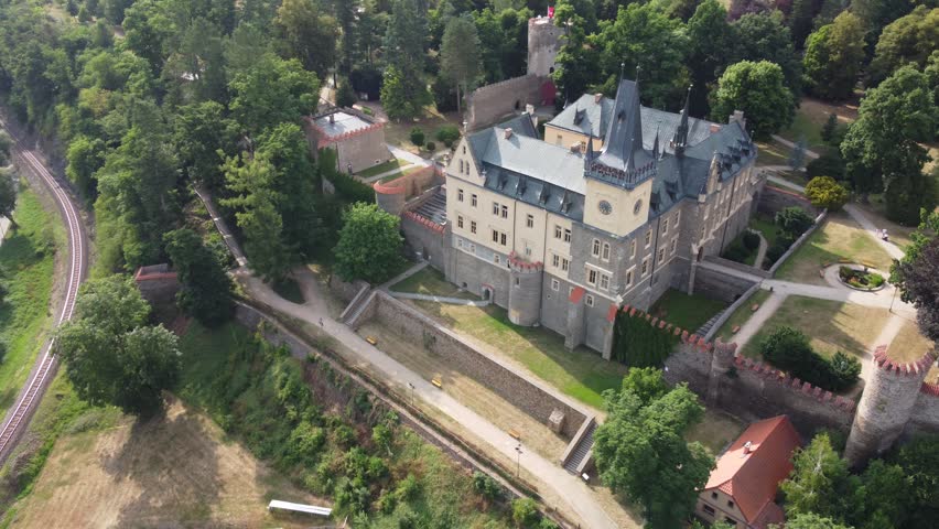 A grand drone view of Zruc nad Sazavou Castle in the Czech Republic showing its fortified stone walls, towers, and surrounding tree-lined parkland