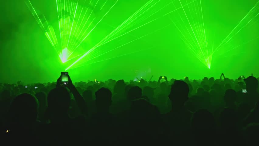 A dark crowd is silhouetted against an intense display of bright green laser beams and lights at Music Festival in Silesia, Poland