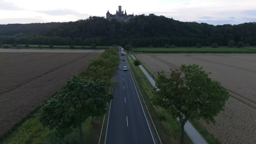 Aerial view along a country road leading toward Marienburg Castle on its forested hill through farm fields
