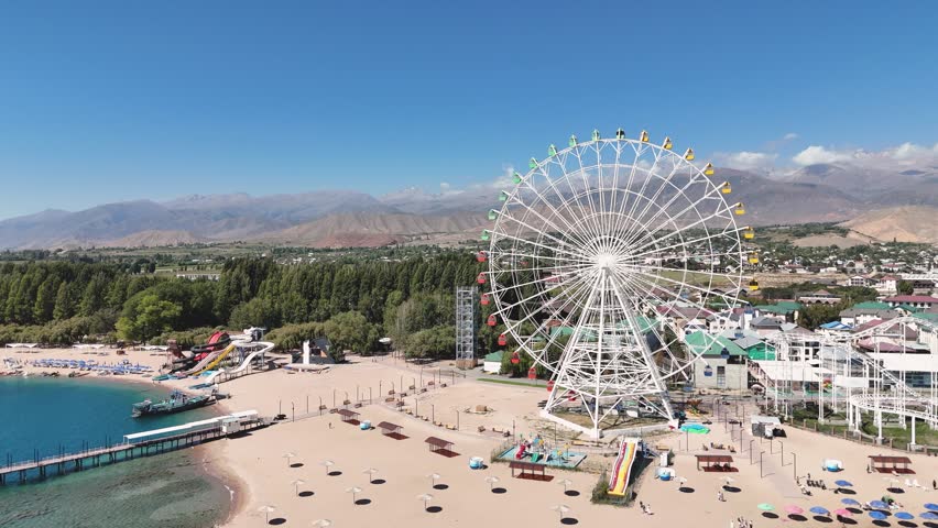 Ferris wheel by Issyk-Kul Lake with scenic mountains in the background, a popular tourist spot.