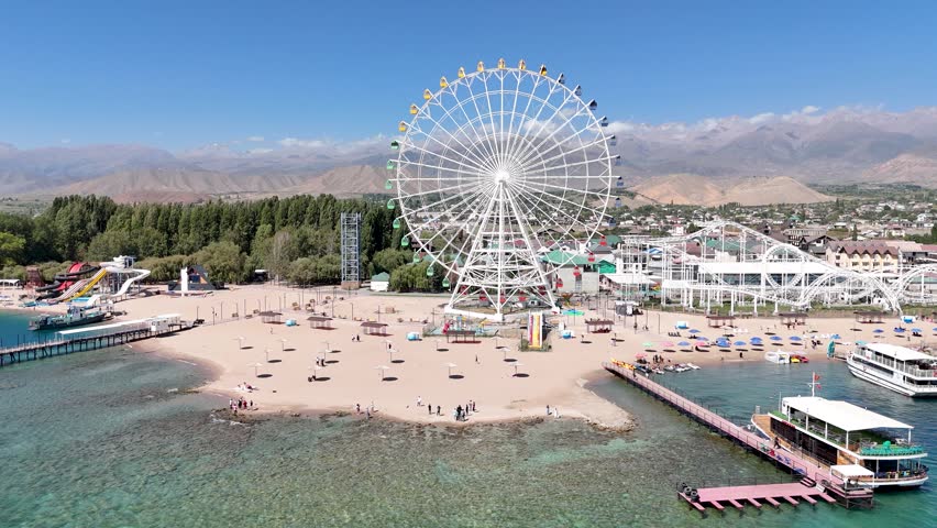 Ferris wheel by Issyk-Kul Lake with scenic mountains in the background, a popular tourist spot.