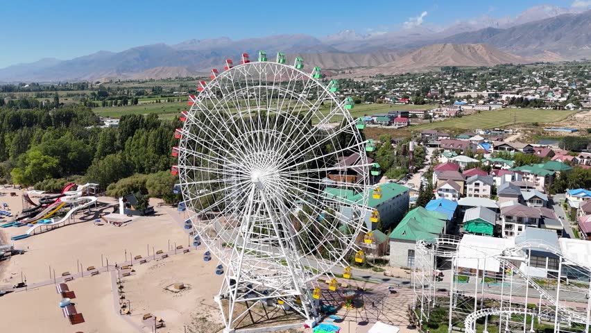 Ferris wheel by Issyk-Kul Lake with scenic mountains in the background, a popular tourist spot.