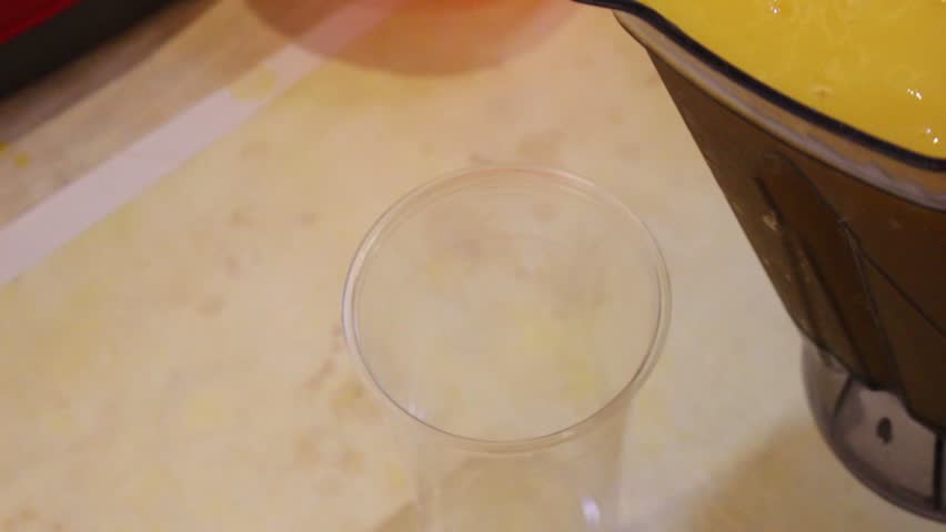 Fresh mango juice being poured into a clear plastic cup, close-up of drink preparation with a smooth flow, refreshing citrus drink, food service, lifestyle footage.