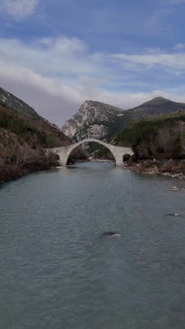 A vertical drone footage of the historic Plaka Arch Bridge, spans the Arachthos River in the Epirus region of Greece