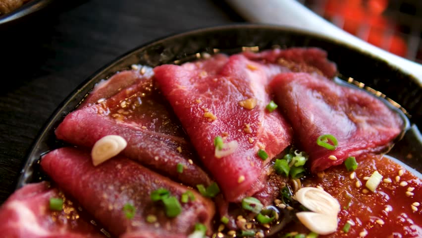 Close-up captures fresh raw beef being grilled at a Korean barbecue restaurant.