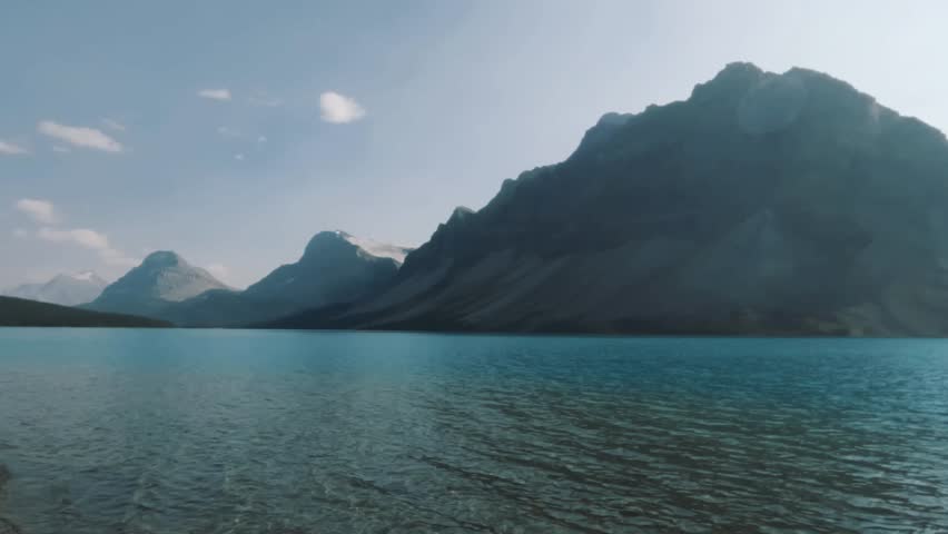 A view of Bow Lake in Banff National Park, Alberta, Canada. The crystal-clear blue waters reflect the towering mountain peaks and soft morning light