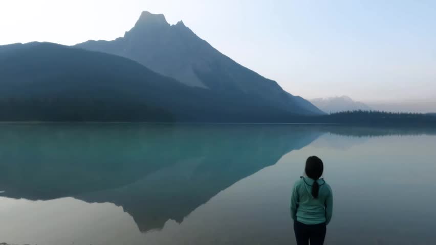 A hiker standing at the shore of Emerald Lake in Yoho National Park, British Columbia. The water mirrors the surrounding peaks and evergreen forest