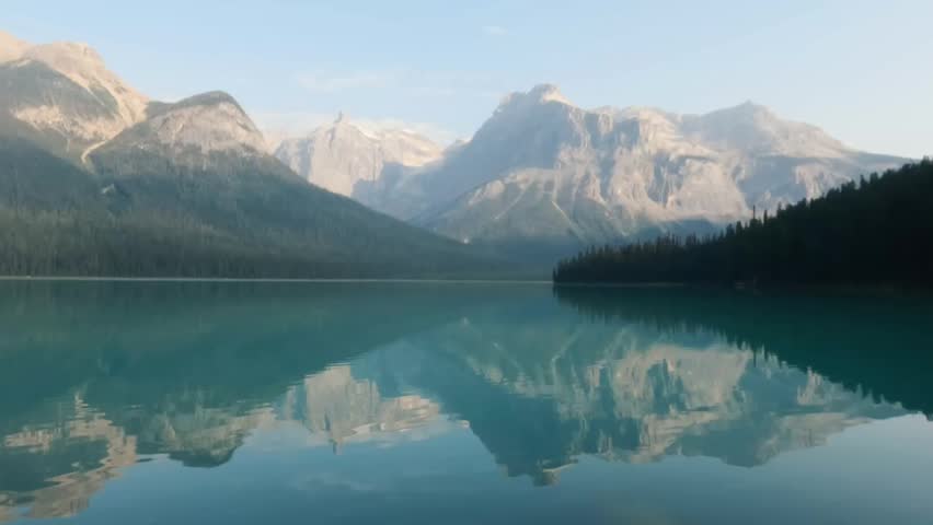 A serene view of Emerald Lake with rocky peaks and dark forest during calm morning in Yoho National Park, British Columbia