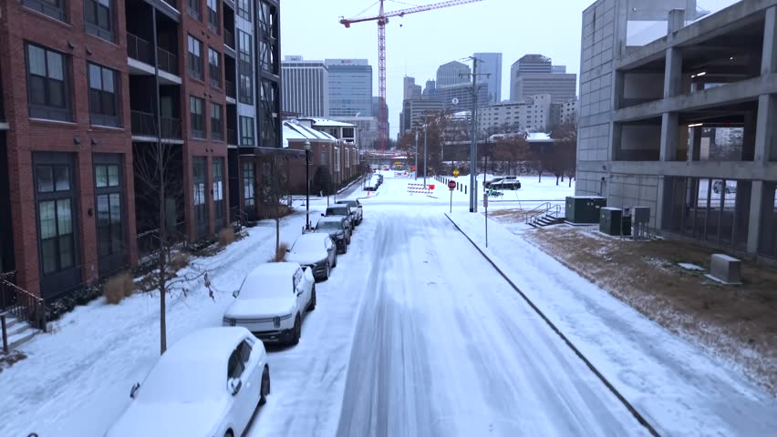 Rising Aerial View Of A Snow-covered Downtown Nashville Street With Apartments, A Crane And City Skyline.