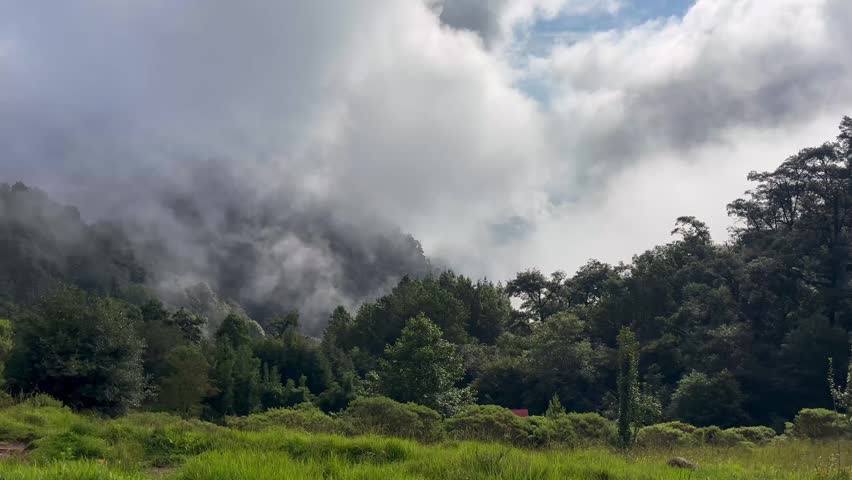 4K landscape footage of heavy fog and white clouds moving through lush green mountain ridges during a bright morning in the Sierra of Honey, Puebla, Mexico.