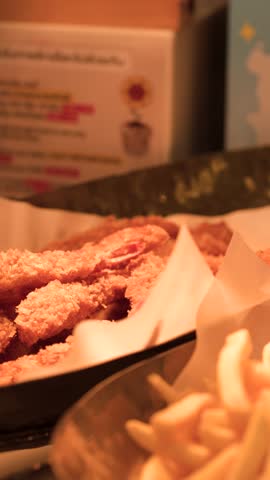 Close-up shot of metal tongs selecting breaded fried shrimp from a warm buffet display.