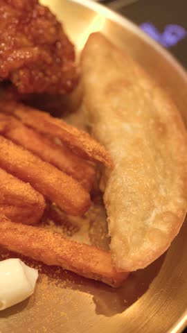 Close-up shot of crispy fried chicken, seasoned fries, and dumplings on a brass plate.