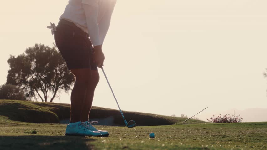 A golfer plays a chip straight into the setting sun as light flares around the silhouette, captured in slow motion, suited to dramatic golf and lifestyle promos.