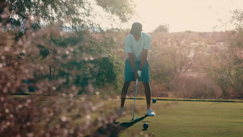 African American golfer hits iron shot on tree lined par 3 tee box at twilight, bright sun flare behind him through pink blooms in slow motion, 4k 800fps golf swing
