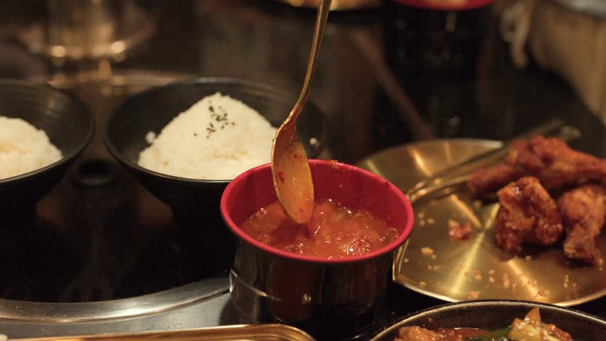 Close-up shot of spicy sauce poured onto rice beside fried chicken in warm restaurant lighting.
