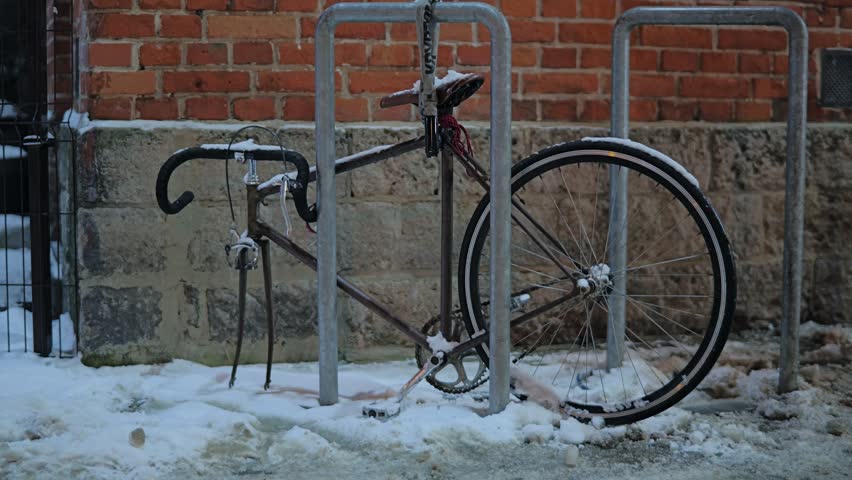 Passerby walks past bicycle missing its front wheel locked to a public bike rack