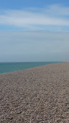 A minimalist cinematic shot of the iconic Chesil Beach pebble shoreline in Weymouth, Dorset. A serene coastal landscape featuring the English Channel and a vast stone beach.
