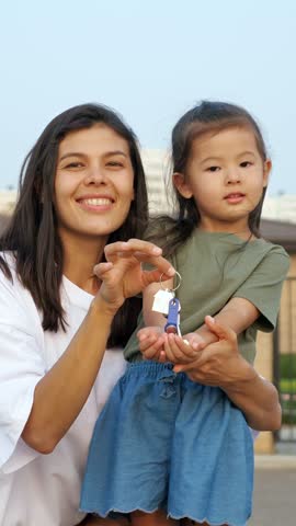 Joyful single mother and her adorable little daughter proudly showing the keys to their new home, celebrating a fresh start and the dream of homeownership becoming a reality