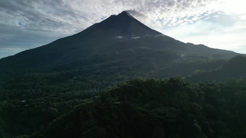 Dolly out drone shot captures the majestic Karangetang volcano in Siau Islands. The active peak towers toward clouds under bright morning sunlight in North Sulawesi.