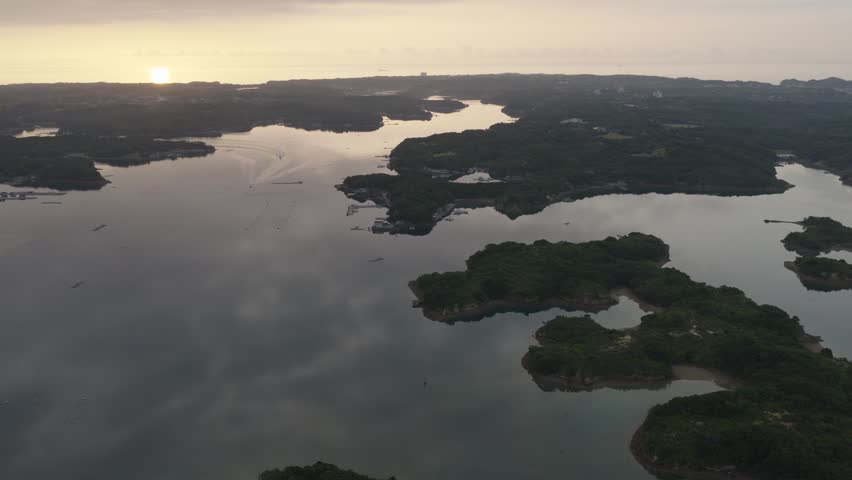 Sunrise aerial view of Ago Bay with golden morning light over forested islands and calm water in Shima, Mie Prefecture, Japan.