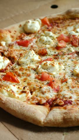 Person hand reaches into cardboard takeout box picks up delicious slice of freshly baked pizza topped with mozzarella cheese tomatoes aromatic oregano. Hand taking slice fresh pizza from cardboard box