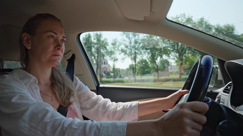 Confident woman sitting behind the steering wheel of her car, commuting to work through the city on a bright and sunny summer day, showcasing a daily routine and modern lifestyle
